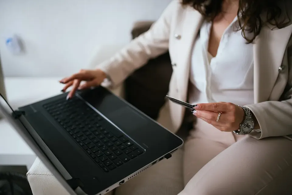 Mężczyzna w garniturze trzyma kartę płatniczą i kupuje online przy laptopie